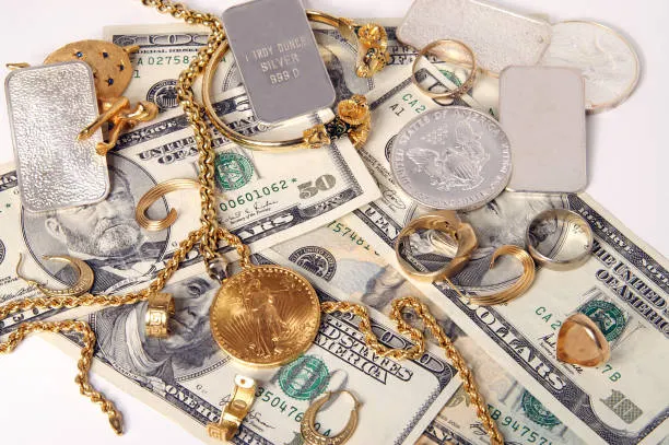 Gold jewelry, silver bars, and gold coins spread across cash on a table
