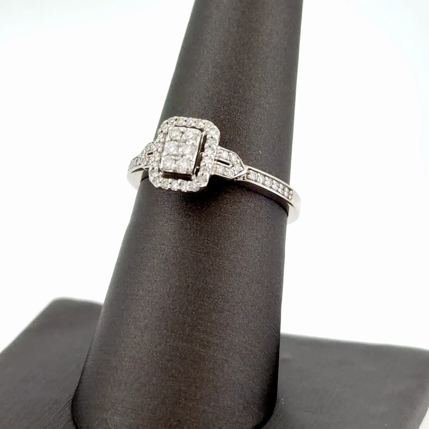 Diamond cluster engagement ring with a rectangular halo and pavé band on a black ring display