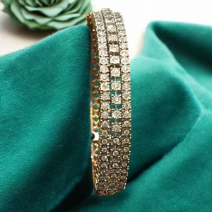 Gold bangle bracelet set with three rows of round diamonds on teal fabric