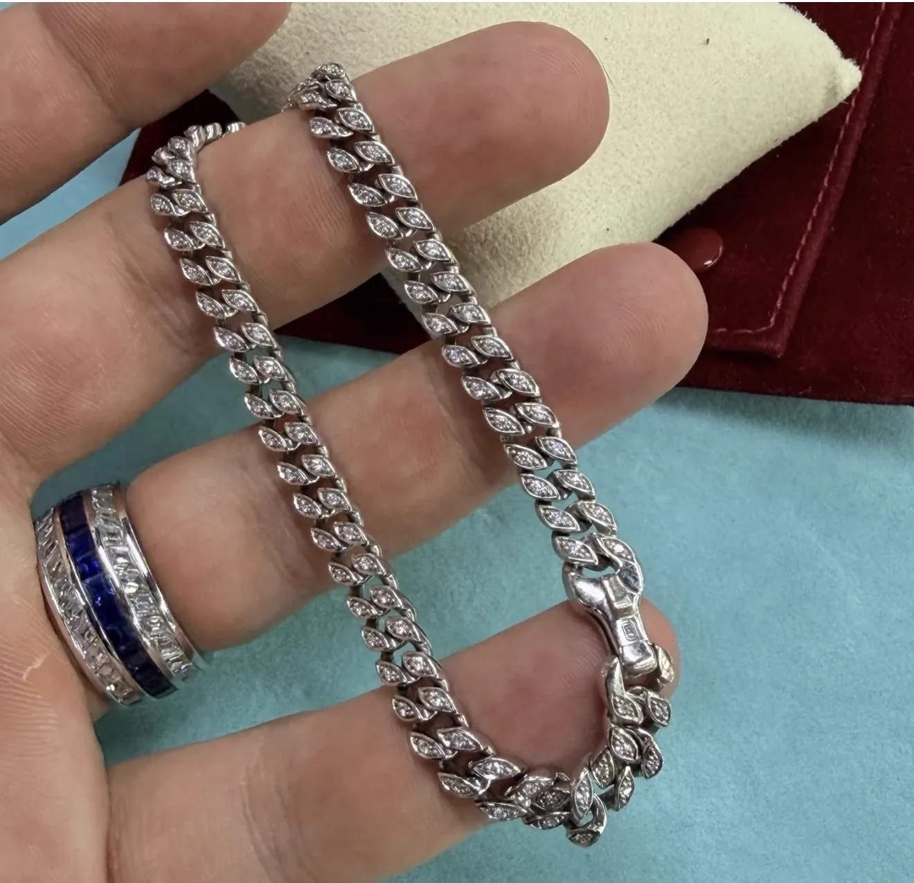 Pavé diamond Cuban link bracelet with a box clasp draped over fingers, worn with a sapphire and diamond channel-set band