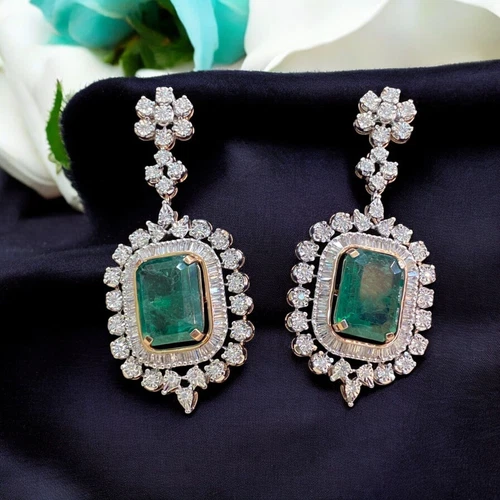 Emerald and diamond drop earrings with baguette and round diamond halos on black velvet