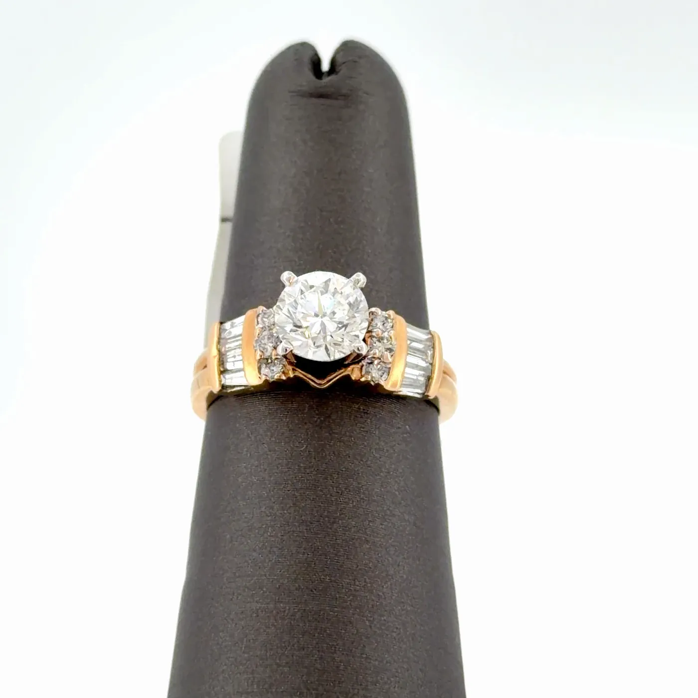 Yellow gold engagement ring with a round brilliant center diamond, round side diamonds and tapered baguettes on a black ring display