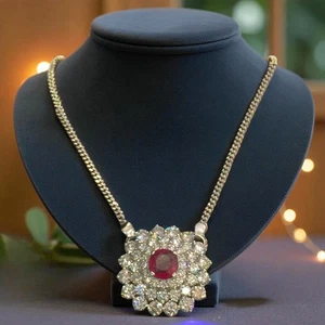 Round ruby set in a cluster of round diamonds on a gold chain displayed on a dark jewelry bust