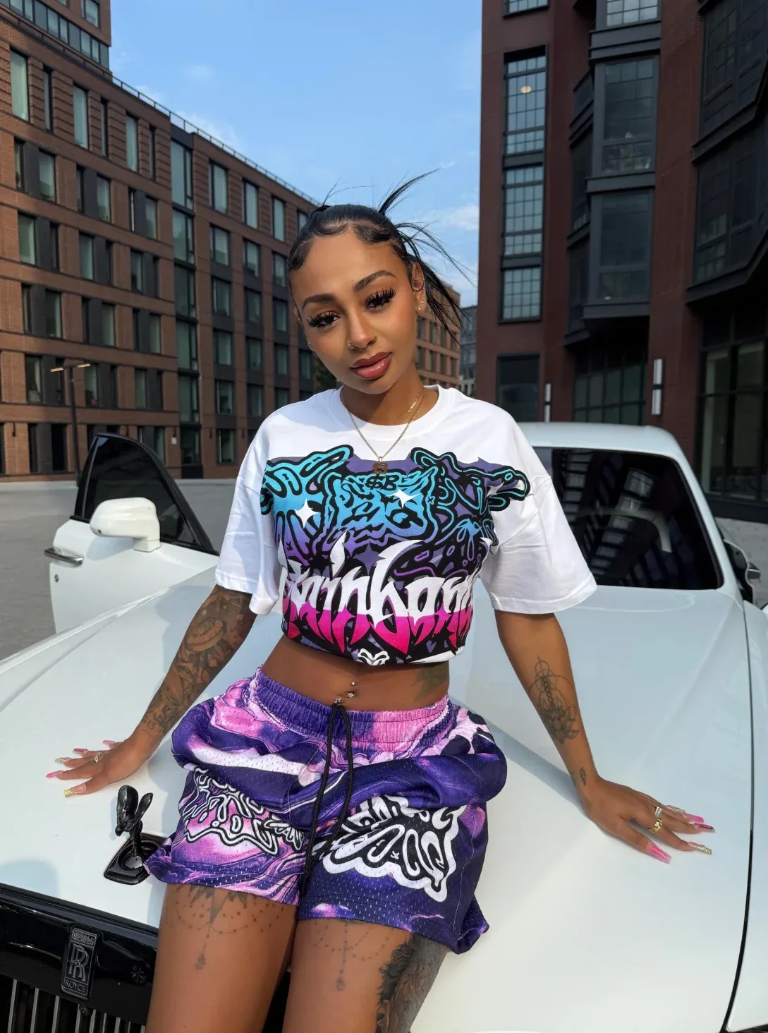 SB Studios matching graphic crop top and shorts set styled with jewelry and a luxury car