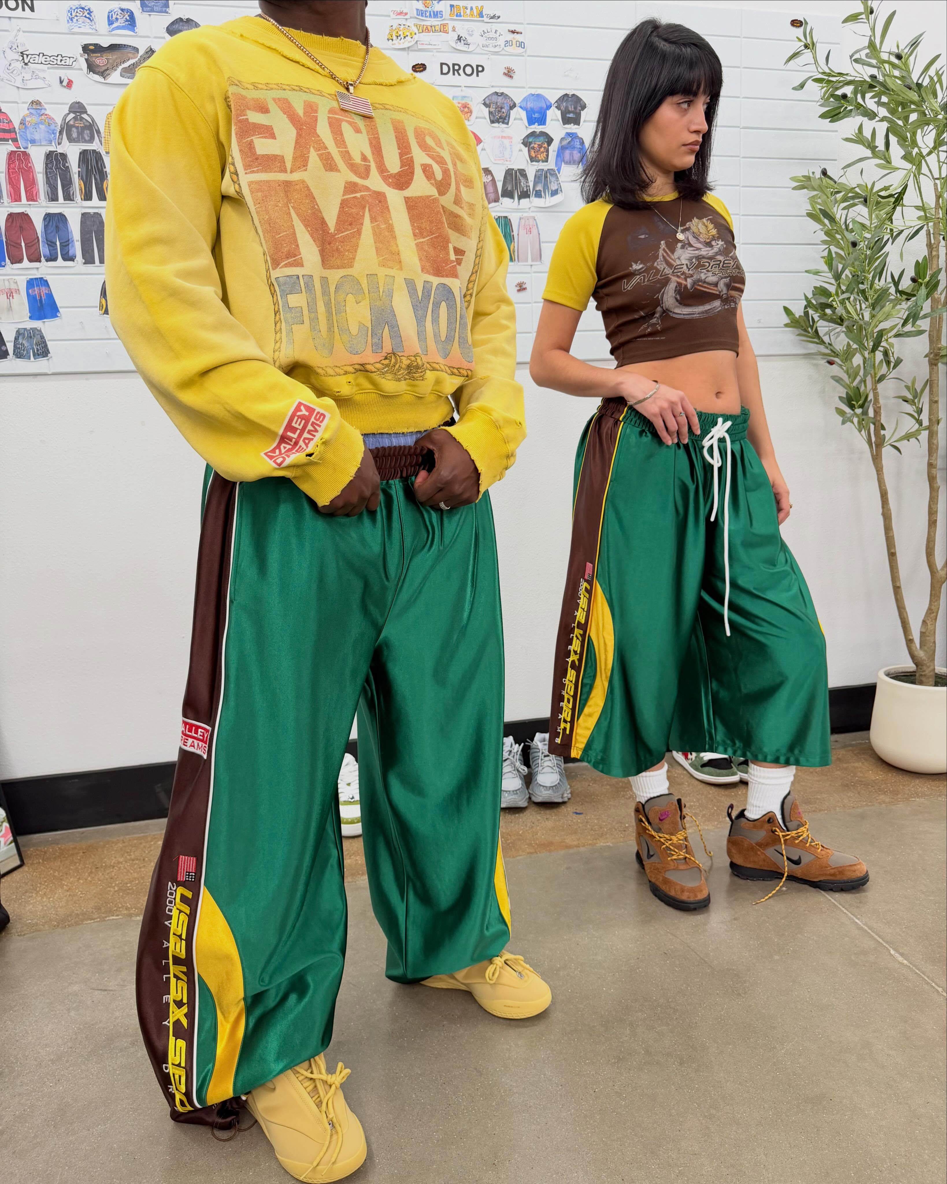 Two models wearing Valley Dreams VSX Sport graphic sweaters and green track pants